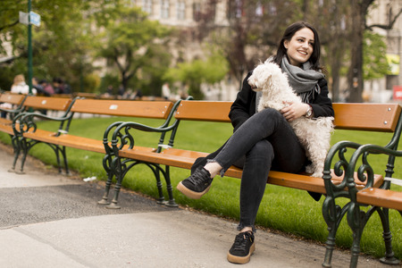 Young woman sitting in the park and holding a small dog in her lapの写真素材