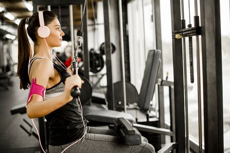Young woman exercises on an exercise machine at the gym listening to music