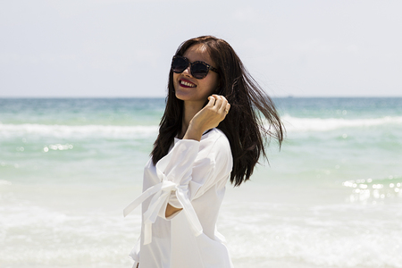 Pretty young vietnamese woman in white dress with sunglasses on the tropical beachの写真素材