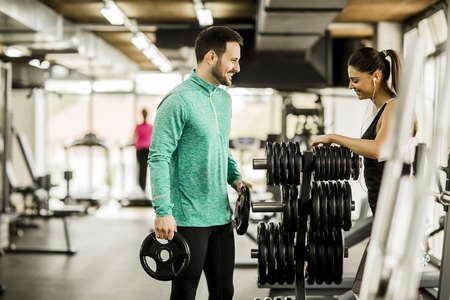 Young woman exercise with weights in the presence of trainer in the gymの写真素材