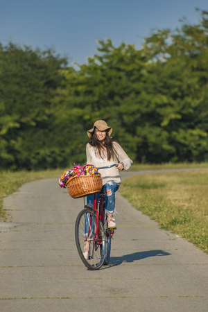 Young smiling woman rides a bicycle with a basket full of flowers in counrtysideの写真素材