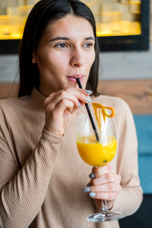 Young woman drinking orange juice in cafeの写真素材