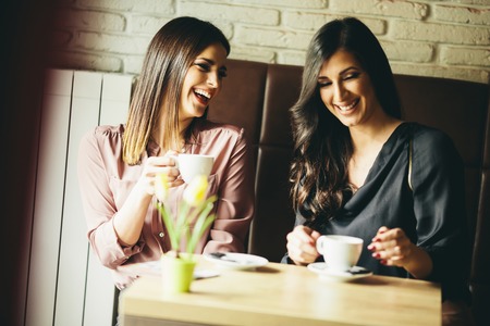 View at two young female friends sitting in a cafe and drink coffeeの写真素材