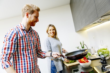 Happy young couple have fun in modern kitchen indoor while preparing vegetables food for lunchの写真素材