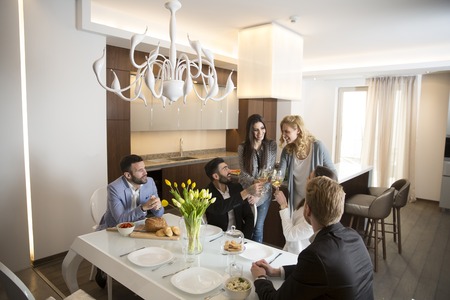 Group of young friends having dinner at home and toasting with white wine