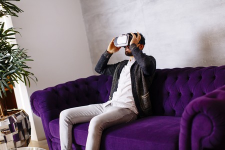 Closeup of bearded young man wearing virtual reality goggles in modern roomの写真素材