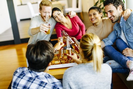 Group of young people eating pizza and drinking cider in the modern interiorの写真素材