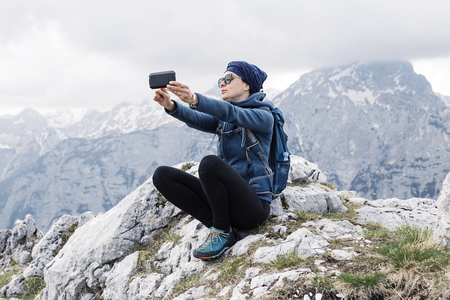 Female hiker making a selfie with her smart phone with hills in backgroundの写真素材
