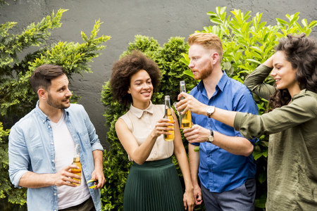 Young smiling people stand outside and toast with cider in the hands outdoorの写真素材
