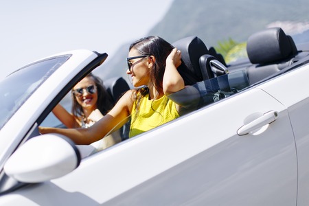 Two happy friends in white cabriolet car driving everywhere and looking for freedom and funの写真素材