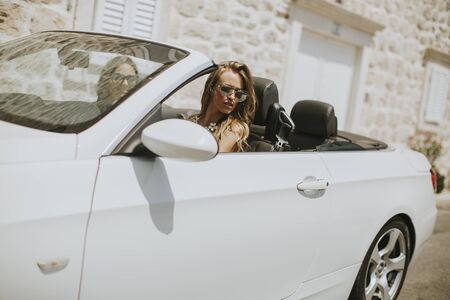 Two happy friends in white cabriolet car driving everywhere and looking for freedom and funの写真素材