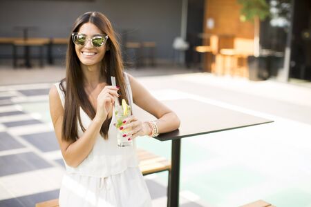 Pretty young woman drinking by the swimming pool on a sunny summer dayの写真素材