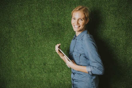 Pretty young woman with tablet by the green wallの写真素材