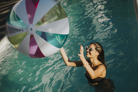 Young womans playing with a ball in the swimming pool at sunny dayの写真素材