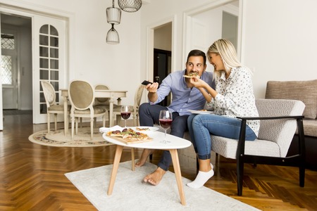 Young couple enjoying eating pizza and watching tv at homeの写真素材