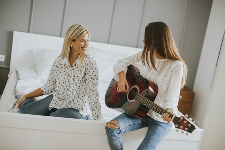 Two young women with acoustic guitar on bedの写真素材