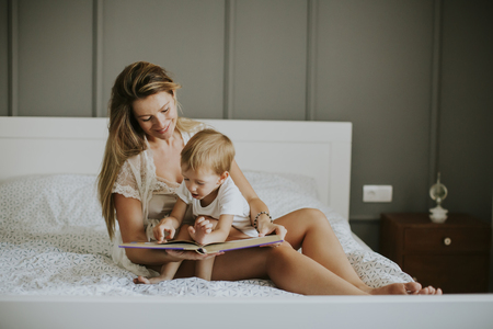 Mother and little boy reading book in bed at homeの写真素材