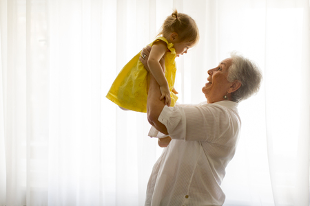 Grandmother holding little granddaughter in the room at homeの写真素材
