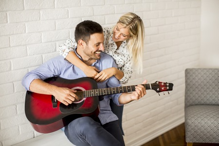 Loving couple with guitar  in the room at homeの写真素材