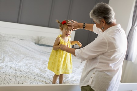 Grandma plays with a little granddaughter  on the bed in the roomの写真素材