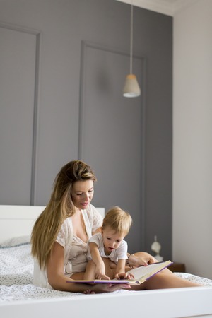 Mother and little boy reading book in bed at homeの写真素材