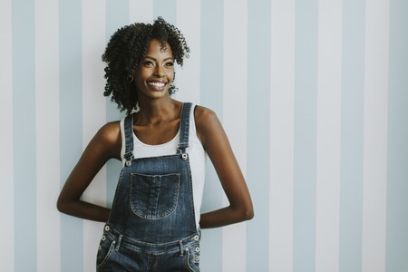 Pretty African American woman posing in jeans trousers by the wall in the room