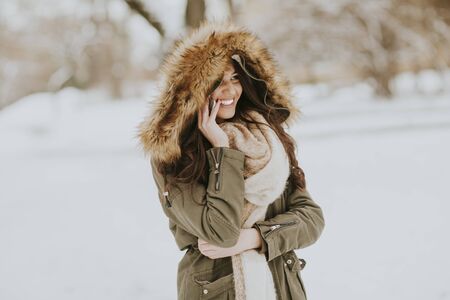 Smiling young woman using phone in park at cold winter day