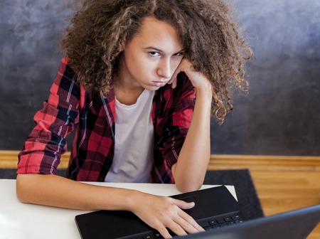 Indisposed teenage girl sitting in front of laptop computer at homeの写真素材