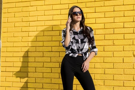 Portrait of a chic woman using mobile phone  in front of a yellow wall