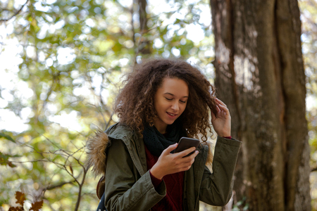 Portrait of curly hair teen girl with smartphone in autumn forestの写真素材
