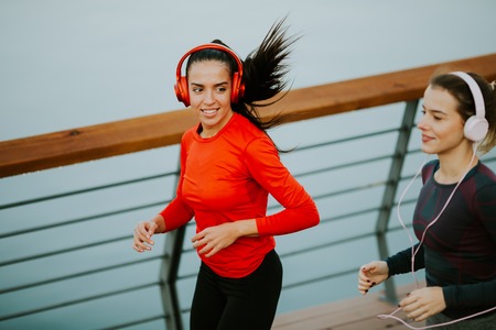 Two young women running by the river in the morningの写真素材