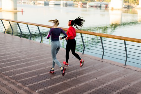 Two young women running by the river in the morningの写真素材
