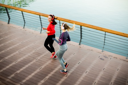Two young women running by river in the morningの写真素材