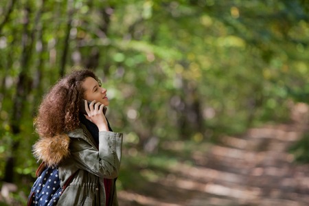 Portrait of curly hair teen girl with smartphone in autumn forestの写真素材