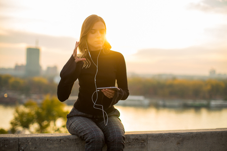 Portrait of trendy young woman listening music from smartphone outdoor at sunsetの写真素材