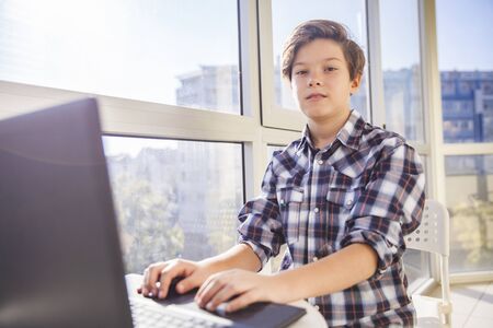 Portrait of teen boy using laptop by windowの写真素材