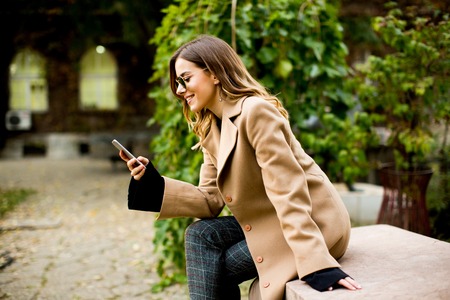 Side view at young woman sitting outdoor and using mobile phoneの写真素材