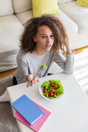 Top view at curly hair teen girl eating salad in the roomの写真素材