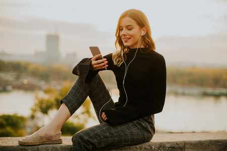 Trendy young woman listening music from smartphone outdoor at sunsetの写真素材