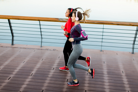 Two young women running by river in the morningの写真素材