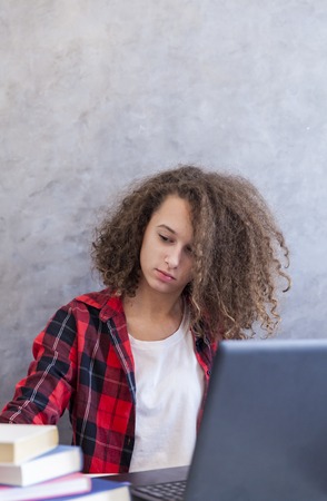 Portrait of curly hair teen girl websurfing internet on laptop at homeの写真素材