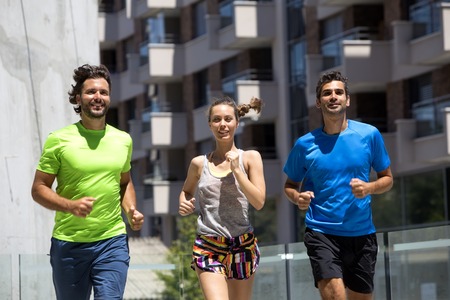 Two young men and woman running in urban enviroment at hot summer dayの写真素材