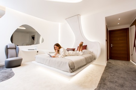 Young woman in silk sleeping dress using digital tablet in modern bedroomの写真素材