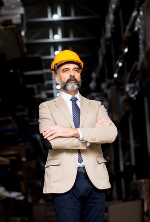 Portrait of handsome businessman in suit with helmet in a warehouseの写真素材