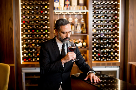 Handsome elegant businessman drinking red wine in barの写真素材