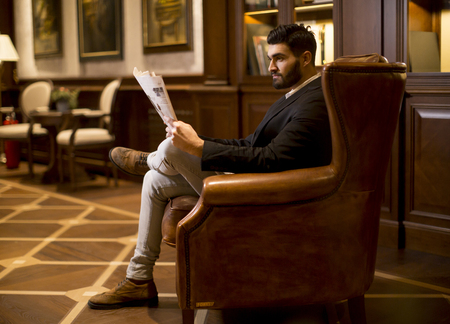 Modern businessman reading newspaper and sitting on sofaの写真素材