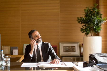 Portrait of senior bearded businessman using mobile phone in modern officeの写真素材