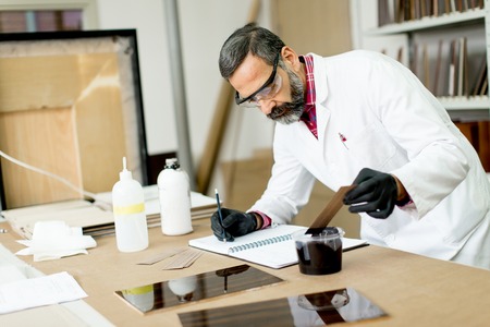 Handsome mature engineer testing colors on wooden specimens in the furniture factoryの写真素材