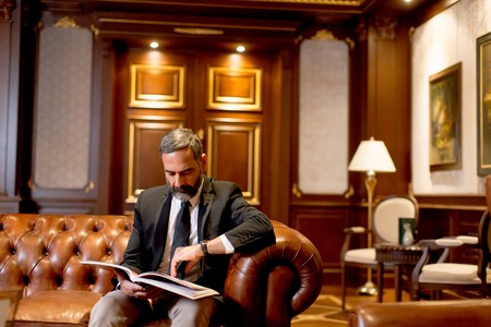 Handsome middle-aged businessman reading book on sofa