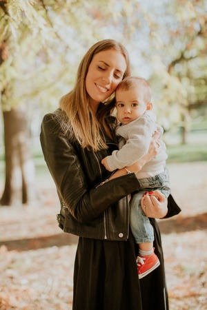 Young mother and baby boy in autumn park at sunny dayの写真素材